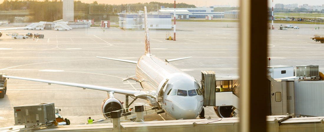 Vista desde el interior de una terminal de aeropuerto, mirando a través de una ventana la cabina y el morro de un avión estacionado en la puerta.