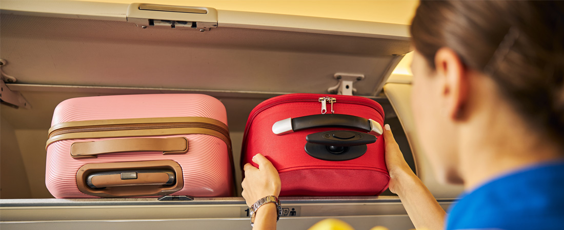 Azafata de vuelo colocando equipaje de mano en el compartimento superior