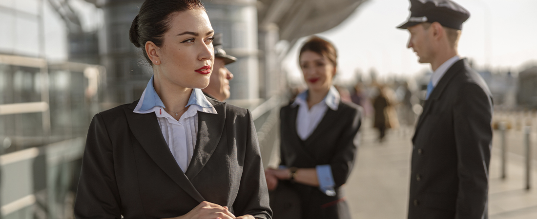 Un grupo de TCP (Tripulantes de Cabina de Pasajeros) con uniforme oficial de color oscuro, conversando seriamente en una pasarela de embarque o terminal de aeropuerto.